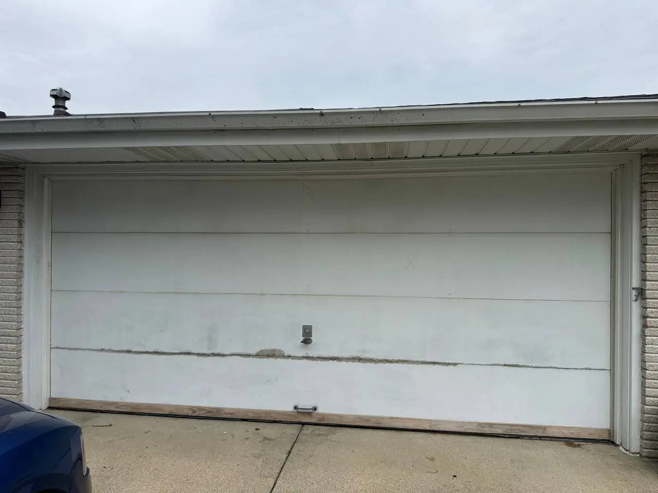 Old white flat-panel double garage door with a wood strip along the bottom